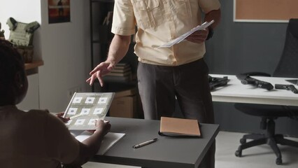 Medium tracking shot of Caucasian military professor in formalwear distributing educational workbooks on shooting to diverse cadets during class in academy