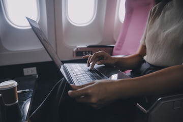 Asian woman passenger sitting in airplane near window and reading news from social networks or...