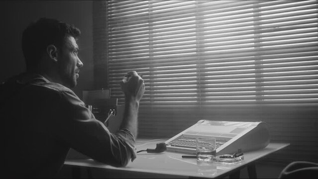 Monochrome rear view of bearded Caucasian smoking man sitting at table thoughtfully looking at window and then checking diary indoors