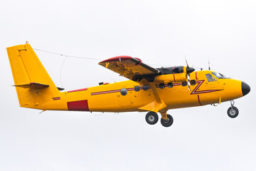 Bright yellow twin engine aircraft flying by. High wing airplane with red stripe and fixed landing...
