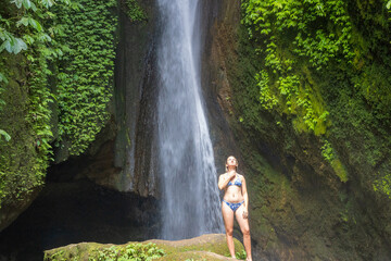 Fototapeta na wymiar A young woman in a swimming suit at Leke Leke waterfall in lush tropical forest, Bali, Indonesia