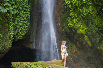 A young woman in a swimming suit at Leke Leke waterfall in lush tropical forest, Bali, Indonesia