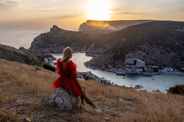 Woman sunset sea mountains. Happy woman siting with her back on the sunset in nature summer posing...