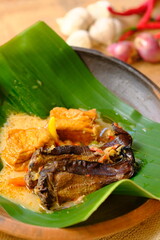 Mangut Ikan Asap is Traditional Indonesian cuisine made of smoked stingray, coconut milk, tofu, chilies and spices. Served on a pottery plate covered with banana leaves. Indonesian food. 