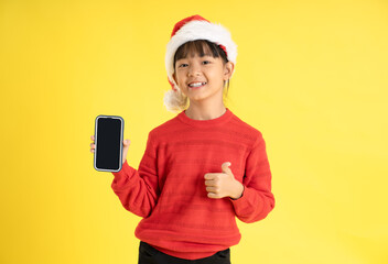 Image of an Asian girl wearing a Christmas sweater and hat , holding phone and posing on a yellow background