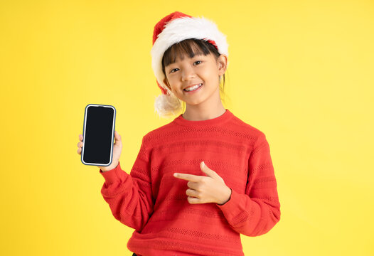 Image of an Asian girl wearing a Christmas sweater and hat , holding phone and posing on a yellow background