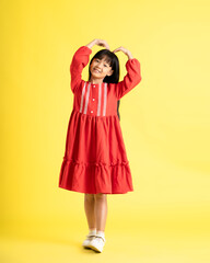full body image of asian kid girl wearing dress and posing on yellow background
