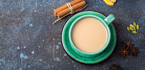 Indian tea hot drink with milk and spices in rustic green teacup with ingredients for making masala...