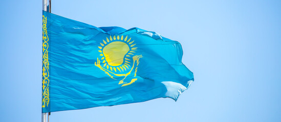The flag of Kazakhstan is fluttering in the wind against the blue sky. The flag is located on the...