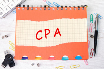 A CPA, a Certified public Accountant word is written on a sheet in a cage lying on a notebook on the table next to stationery