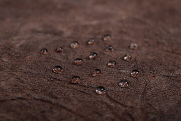 Round water drops on dark brown leather texture, side view, soft focus macro pattern