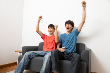 Two boys sitting on sofa and watching TV together. Isolated on white background