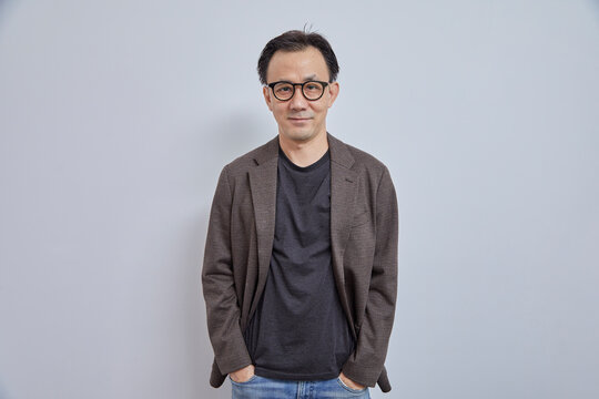 Handsome Asian Businessman In Suit With Eyeglass Smile And Look At Camera On Grey Background.