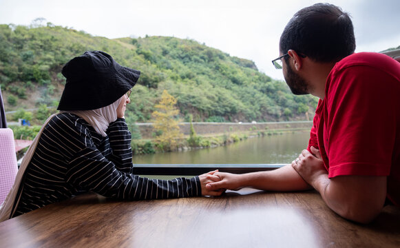 Young muslim couples felling love while looking at natural lake from restaurant table during vacation holding eac other hand