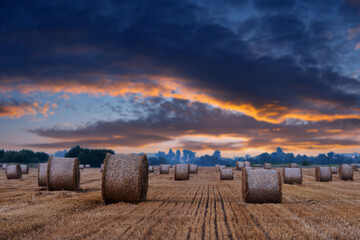 The sun setting behind an agricultural expanse adorned with rounded hay bundles. Rural landscape...