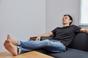 Old Asian man take a nap on grey sofa in a room.