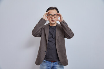 Portrait of stressed Japanese businessman in suit having headache on grey background.