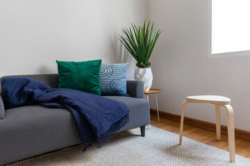 Scandinavian interior decoration of grey sofa with blue and green pillow on it. Green plant pot on side table.