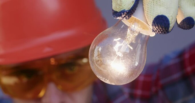 Worker equipped with goggles functioned as technician as well as troubleshooter meticulously check lightbulb to ensure proper function. Closeup at bulb that lights.