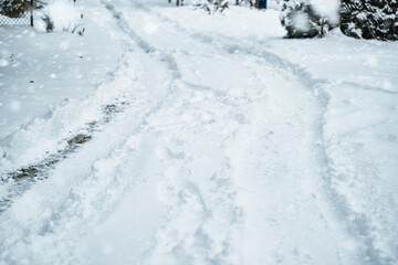 A plowed road in a snowy landscape. A snowplow has made the road passable. The trees and rocks are covered with white snow. A blizzard has left a thick layer of snow on the ground and the trees.