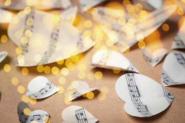 Christmas and New Year music. Hearts cut out from music sheets on wooden background, bokeh effect