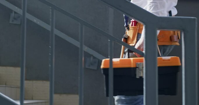 Worker walking across site with necessary equipment. Climbing upward worker with helmet and toolbox ensures well-prepared for work shift