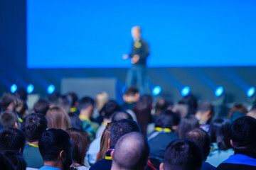 Back view of businesspeople listening to male speaker on stage during global presentation at...