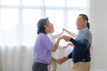Fototapeta premium Asian Older male and females people dance with their partners on a dancing floor in living space. Happy older couple performing get exercise. Joyful carefree retired senior friends enjoying relaxation