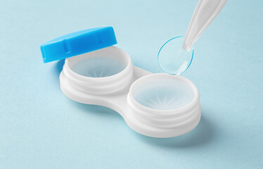 Contact lenses with tweezer and container on light blue background