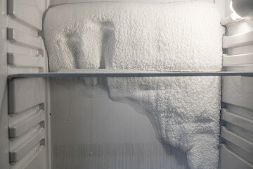 Frozen refrigerator that needs to be defrosted. Block of ice in the empty fridge. empty shelves in...