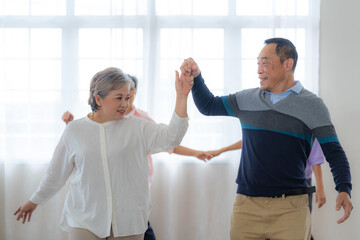 Obraz premium Asian Older male and females people dance with their partners on a dancing floor in living space. Happy older couple performing get exercise. Joyful carefree retired senior friends enjoying relaxation