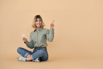 Happy pretty gen z blonde young woman with smartphone, smiling european customer girl with short blond hair pointing aside using mobile cell phone advertising promotion on beige background. Copy space