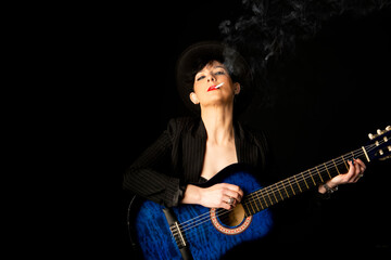Obraz na płótnie Canvas Young beautiful woman in black with a cigarette and an acoustic blue guitar