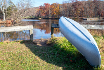 Vintage metal canoe by idyllic autumn lake fall colors trees reflected in water, grass shore with...