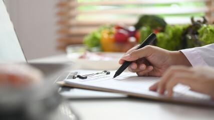 Professional nutritionist sitting at desk with fruit and vegetable working on diet plan - obrazy, fototapety, plakaty