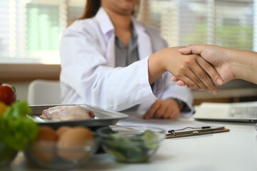 Cropped shot of dietitian in white coat shaking hands with patient at clinic. Health care and right...