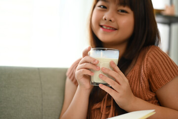 Happy little Asian schoolgirl drinking milk for good health and looking at camera