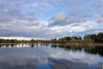Spring landscape with clouds reflected in the water, young trees and shrubs on the horizon