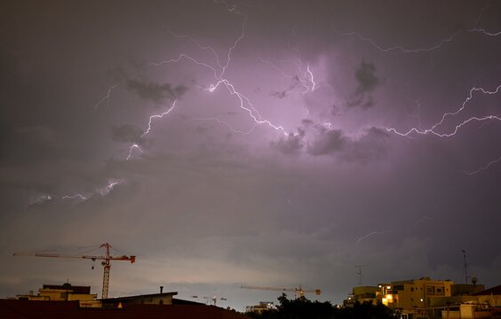 High resolution panoramic night urban image of a thunderstorm with city and cranes in the distance- Israel