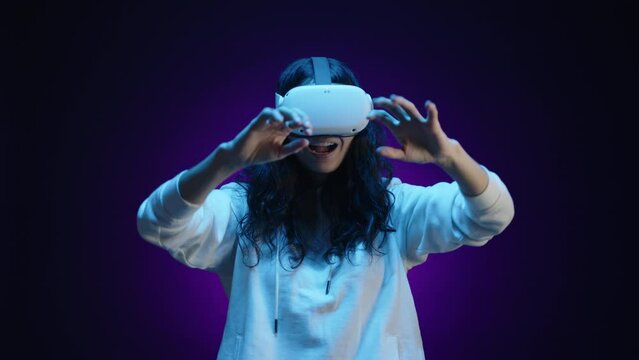 A woman in virtual reality glasses interacts with the virtual world using her hands. She is in a room with a dark purple background illuminated by blue light. High quality 4k footage