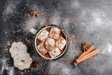 Homemade spicy hot chocolate drink with white marshmallows in enamel cup on wooden table with...