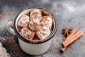 Homemade spicy hot chocolate drink with white marshmallows in enamel cup on wooden table with cinnamon stick, cookies and star anise