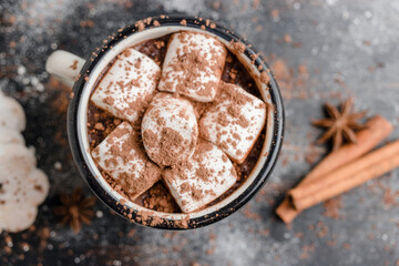 Homemade spicy hot chocolate drink with white marshmallows in enamel cup on wooden table with cinnamon stick, cookies and star anise, top view