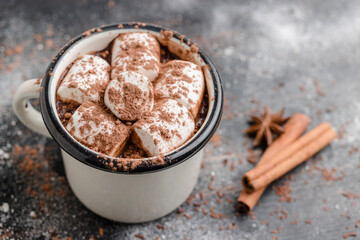 Homemade spicy hot chocolate drink with white marshmallows in enamel cup on wooden table with cinnamon stick and star anise