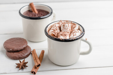 Homemade spicy hot chocolate drink with marshmallows in enamel cup on white wooden table with cinnamon stick, cookies and star anise
