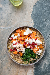 Quinoa with feta, roasted sweet potato, pomegranate and wilted spinach, flat lay on a beige and grey granite background, vertical shot with space