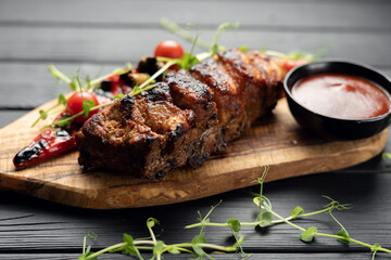 Hot grilled spare ribs from a summer BBQ served with a fresh tomatoes on an wooden cutting board