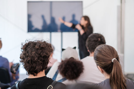 Audience engaging with speaker at a conference, focus on diverse listeners, blurred presenter in background. 