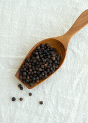 wooden scoop with black peppercorns on a light background