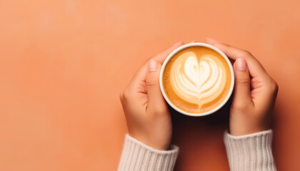 two hands of woman holding cup of coffee with latte ,top view with copy space in peach fuzz color of the year  2024 background - obrazy, fototapety, plakaty